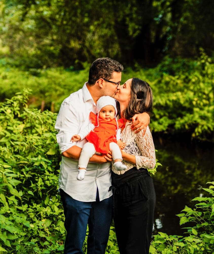 eine Mann und eine Frau halten ihr Baby auf dem Arm und stehen vor einem Fluss in der Natur