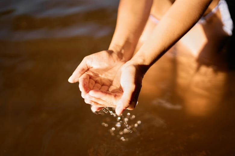 Frau mit einer Hand voll Wasser am See