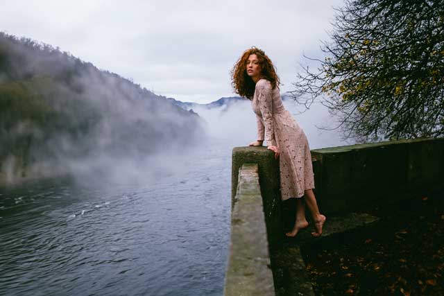 eine Frau im Kleid steht an einer Mauer am Wasser mit KI